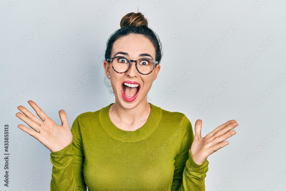 Young hispanic girl wearing casual clothes and glasses celebrating crazy and amazed for success with arms raised and open eyes screaming excited. winner concept Young hispanic girl wearing casual clothes and glasses celebrating crazy and amazed for success with arms raised and open eyes screaming excited. winner concept