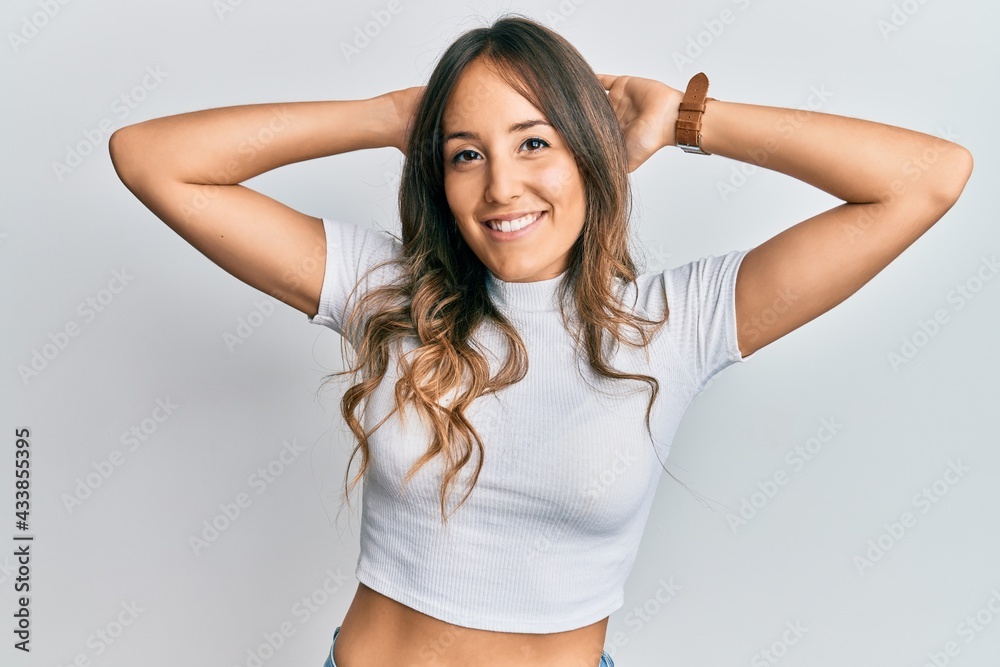Young brunette woman wearing casual white t shirt relaxing and stretching, arms and hands behind head and neck smiling happy Young brunette woman wearing casual white t shirt relaxing and stretching, arms and hands behind head and neck smiling happy