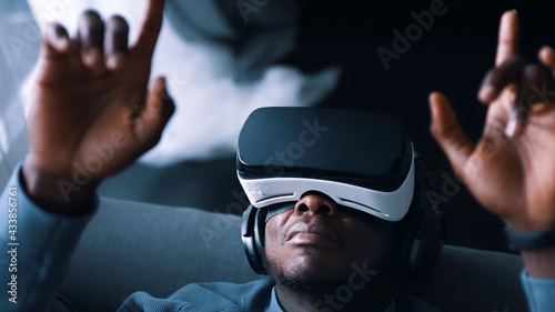 African-American man wearing virtual reality glasses and headset lying on the sofa. Touching the air. Futuristic. High quality photo