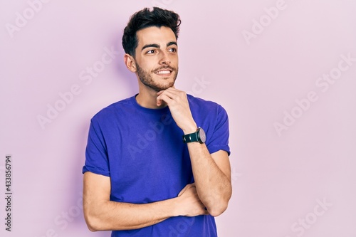 Young hispanic man wearing casual t shirt with hand on chin thinking about question, pensive expression. smiling and thoughtful face. doubt concept.