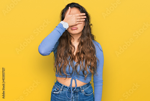 Young hispanic girl wearing casual clothes covering eyes with hand, looking serious and sad. sightless, hiding and rejection concept