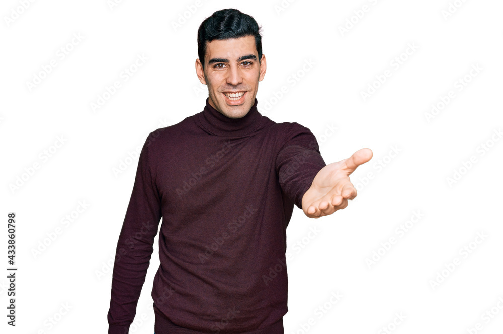 Handsome hispanic man wearing casual turtleneck sweater smiling friendly offering handshake as greeting and welcoming. successful business. Handsome hispanic man wearing casual turtleneck sweater smiling friendly offering handshake as greeting and welcoming. successful business.