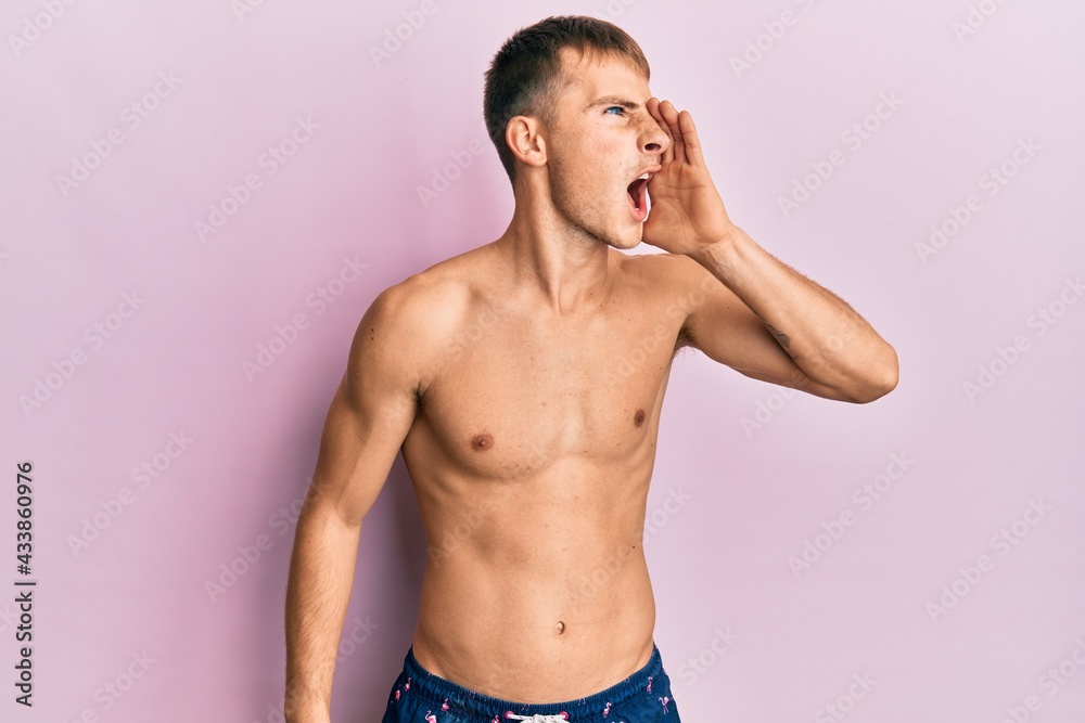 Naklejka premium Young caucasian man wearing swimwear shouting and screaming loud to side with hand on mouth. communication concept.