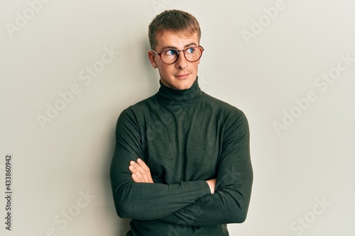 Young caucasian man wearing glasses with arms crossed gesture smiling looking to the side and staring away thinking.