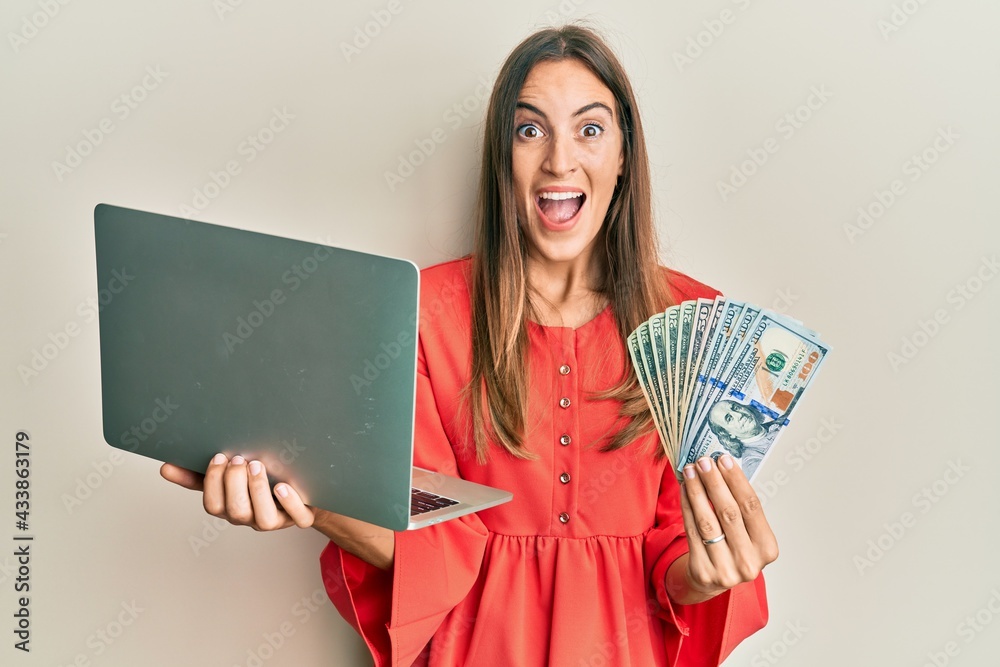 Young beautiful woman working at the office holding dollars celebrating crazy and amazed for success with open eyes screaming excited. Young beautiful woman working at the office holding dollars celebrating crazy and amazed for success with open eyes screaming excited.