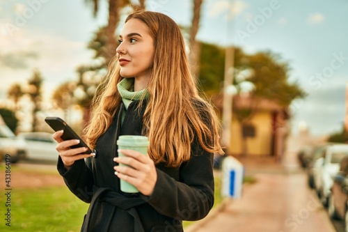 Young blonde girl using smartphone drinking coffee at the city.