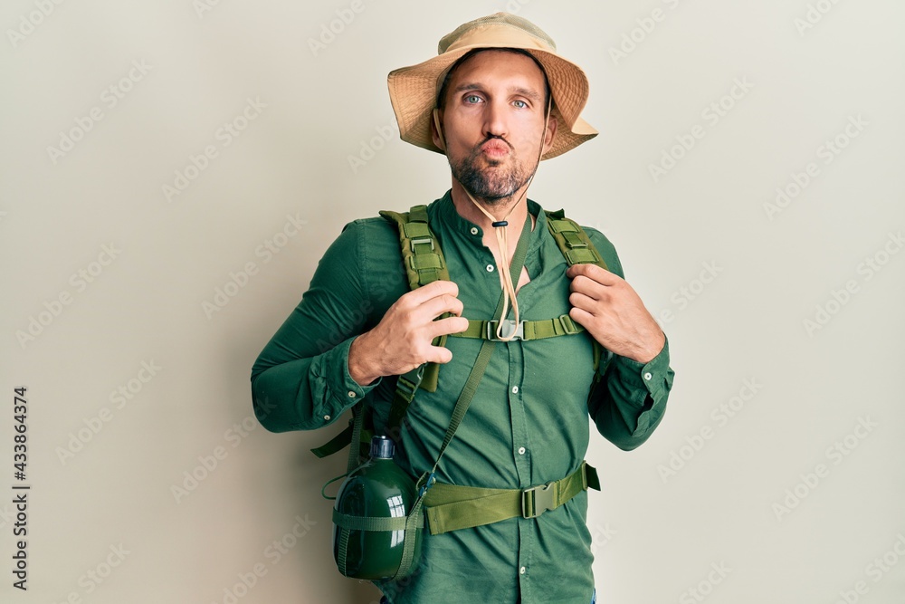 Handsome man with beard wearing explorer hat and backpack looking at the camera blowing a kiss on air being lovely and sexy. love expression. Handsome man with beard wearing explorer hat and backpack looking at the camera blowing a kiss on air being lovely and sexy. love expression.