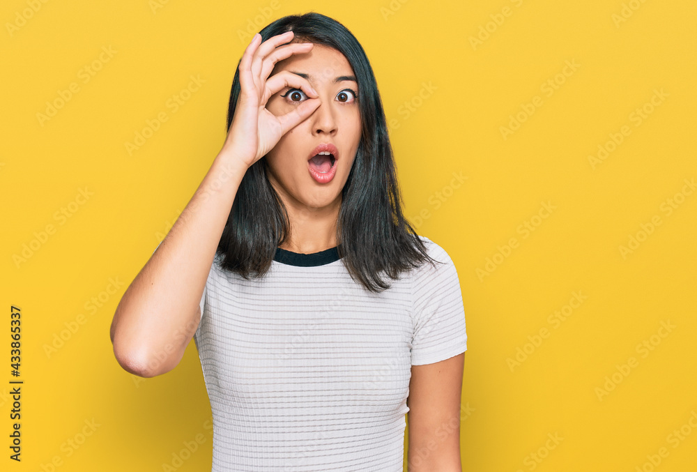 Beautiful asian young woman wearing casual white t shirt doing ok gesture shocked with surprised face, eye looking through fingers. unbelieving expression. Beautiful asian young woman wearing casual white t shirt doing ok gesture shocked with surprised face, eye looking through fingers. unbelieving expression.