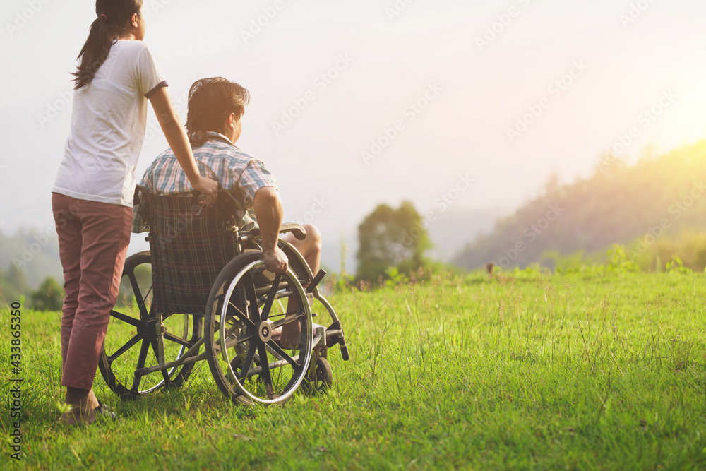 Disabled handicapped man in wheelchair and care helper walking on mountain park. Rear view Disabled handicapped man in wheelchair and care helper walking on mountain park. Rear view