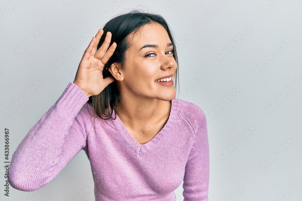 Young hispanic girl wearing casual clothes smiling with hand over ear listening and hearing to rumor or gossip. deafness concept. Young hispanic girl wearing casual clothes smiling with hand over ear listening and hearing to rumor or gossip. deafness concept.