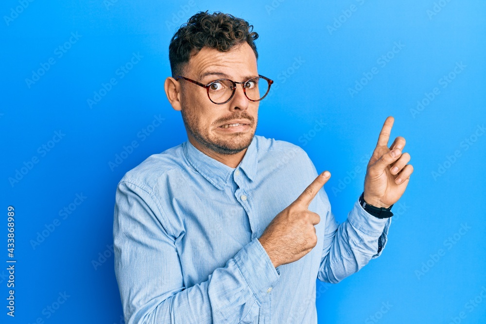 Young hispanic man wearing casual clothes and glasses pointing aside worried and nervous with both hands, concerned and surprised expression Young hispanic man wearing casual clothes and glasses pointing aside worried and nervous with both hands, concerned and surprised expression