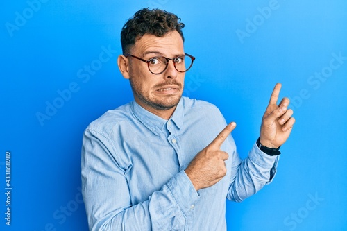 Young hispanic man wearing casual clothes and glasses pointing aside worried and nervous with both hands, concerned and surprised expression