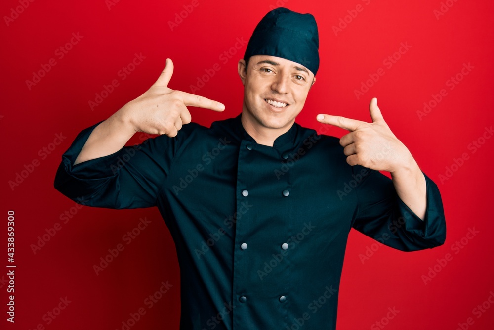 Handsome young man wearing professional cook uniform and hat smiling cheerful showing and pointing with fingers teeth and mouth. dental health concept.