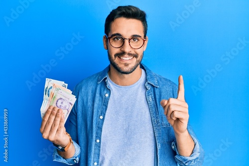Photography Young hispanic man holding singapore dollars banknotes smiling with an idea or q