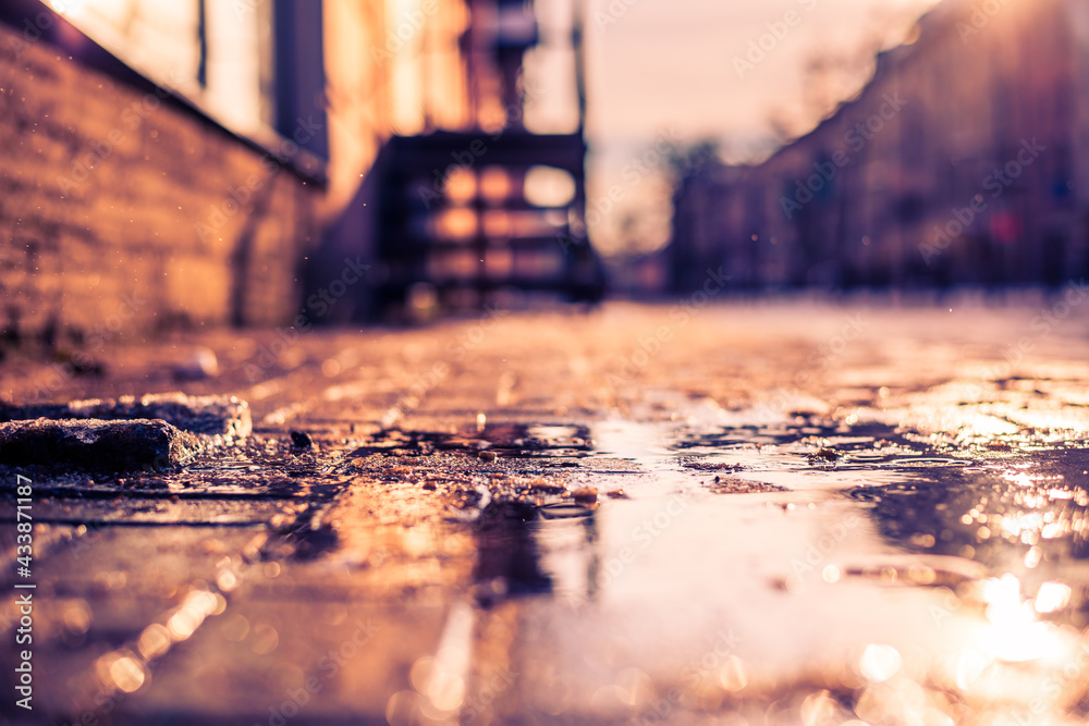 Streets in the late autumn, sidewalk illuminated sun. Close up view from the level of the puddle on the sidewalk Streets in the late autumn, sidewalk illuminated sun. Close up view from the level of the puddle on the sidewalk