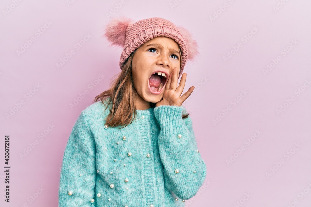 Little beautiful girl wearing wool sweater and cute winter hat shouting and screaming loud to side with hand on mouth. communication concept. Little beautiful girl wearing wool sweater and cute winter hat shouting and screaming loud to side with hand on mouth. communication concept.