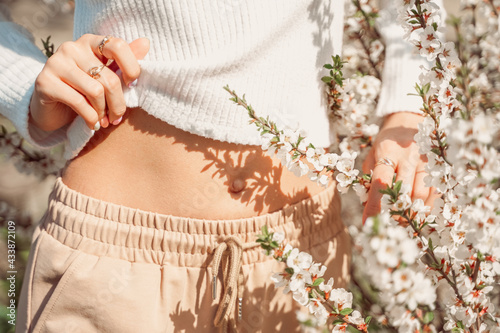 Partial view of beautiful slender woman in delicate clothes posing with hands near her belly and with white flowers in bloom delicate photo, pastel colors. photo