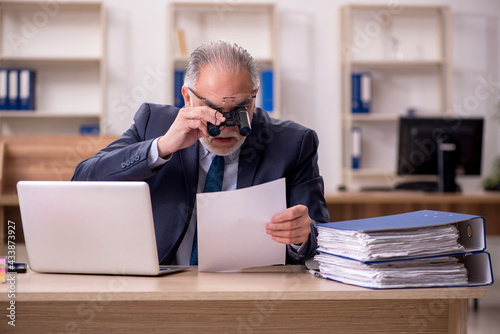 Old male employee auditor holding binoculars at workplace