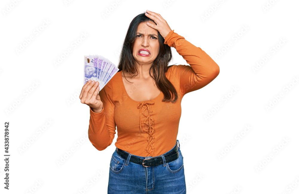 Beautiful hispanic woman holding 20 swedish krona banknotes stressed and frustrated with hand on head, surprised and angry face Beautiful hispanic woman holding 20 swedish krona banknotes stressed and frustrated with hand on head, surprised and angry face
