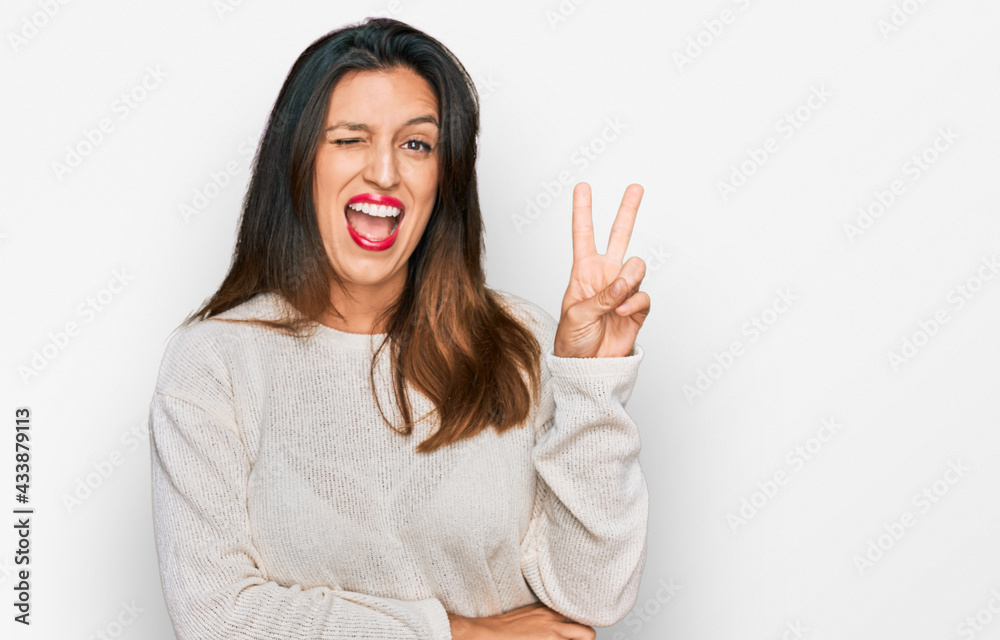 Beautiful hispanic woman wearing casual sweater smiling with happy face winking at the camera doing victory sign. number two. Beautiful hispanic woman wearing casual sweater smiling with happy face winking at the camera doing victory sign. number two.