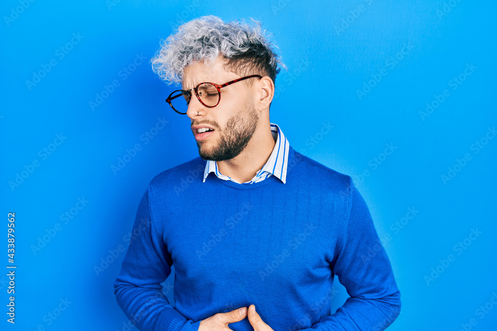 Young hispanic man with modern dyed hair wearing sweater and glasses with hand on stomach because nausea, painful disease feeling unwell. ache concept.