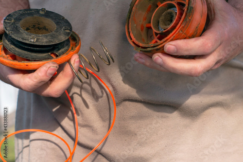 a man winds a new fishing line into the spool of a grass mowing trimmer