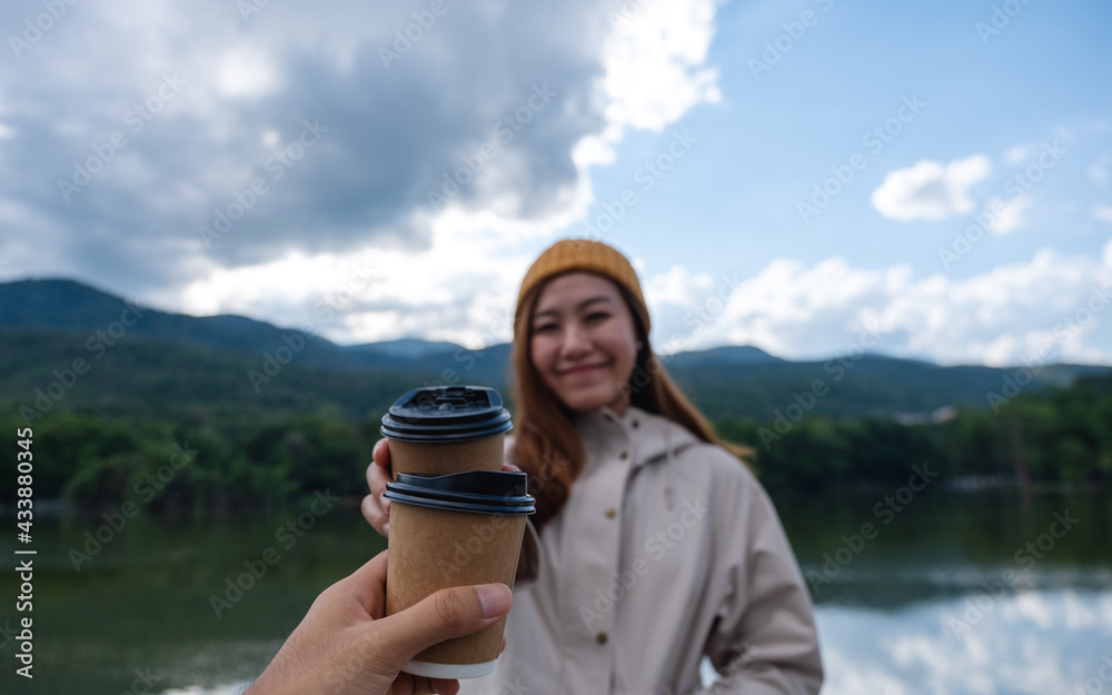 A couple holding and clinking coffee cup together while traveling mountains and the lake