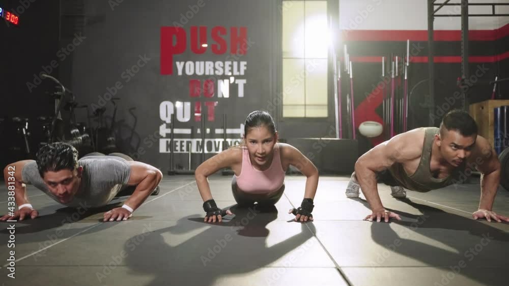 Group of sportsmen doing push up exercises at indoor physical fitness cross-training exercise facility with bright light flare over them
