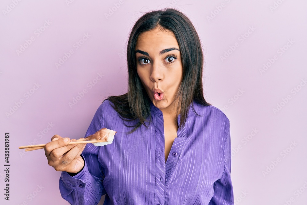 Young brunette woman eating nigiri sushi using chopsticks scared and amazed with open mouth for surprise, disbelief face Young brunette woman eating nigiri sushi using chopsticks scared and amazed with open mouth for surprise, disbelief face