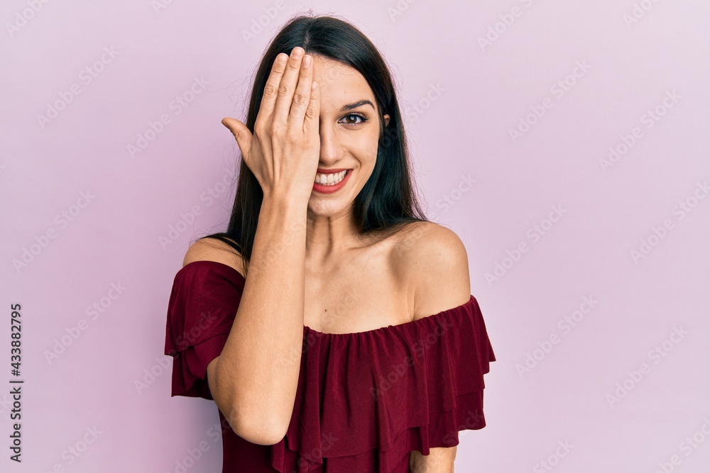 Young hispanic woman wearing casual clothes covering one eye with hand, confident smile on face and surprise emotion. Young hispanic woman wearing casual clothes covering one eye with hand, confident smile on face and surprise emotion.