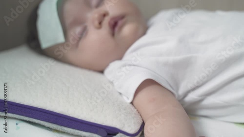 asian baby infant get fever and apply cool patch on forehead sleeping at home after vaccination. cold pad gel healing temperature. baby sick after back from hospital.