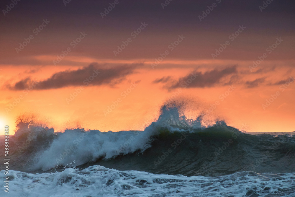 View of a big waves at stormy sea with colorful orange sunset sky background