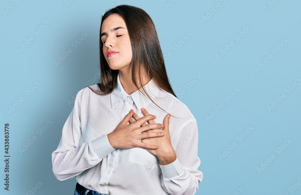 Young brunette teenager wearing business white shirt smiling with hands on chest with closed eyes and grateful gesture on face. health concept. Young brunette teenager wearing business white shirt smiling with hands on chest with closed eyes and grateful gesture on face. health concept.