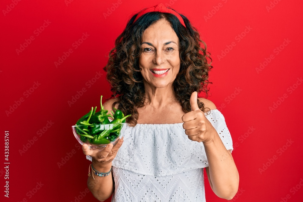 Middle age hispanic woman holding bowl with green peppers smiling happy and positive, thumb up doing excellent and approval sign Middle age hispanic woman holding bowl with green peppers smiling happy and positive, thumb up doing excellent and approval sign