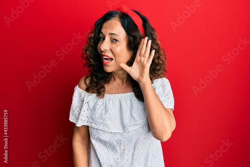 Middle age hispanic woman wearing casual clothes smiling with hand over ear listening an hearing to rumor or gossip. deafness concept.