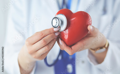 A doctor with stethoscope examining red heart, isolated on white background photo