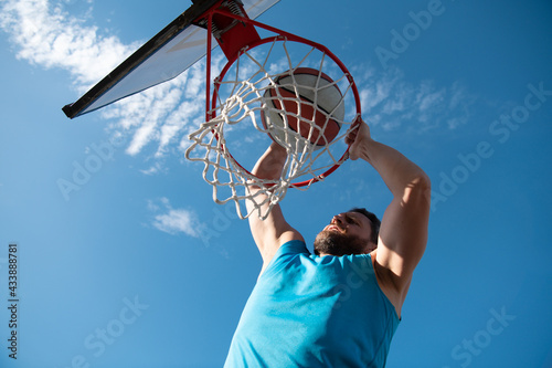 Basketball player. Sports and basketball. A young man jumps and throws a ball into the basket. Blue sky and court in the background.