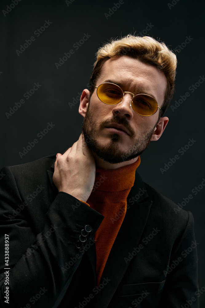 Fototapeta premium fashionable blond man in a sweater and a jacket on a dark background tilted his head to the side 