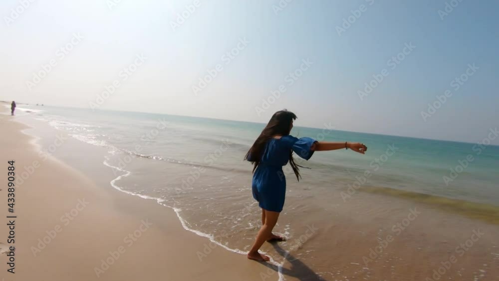 Indian happy young woman dancing in shoreline waves rolling over beach. Excited and happy , pure happiness from being one with nature. Enjoy summertime vacation Indian happy young woman dancing in shoreline waves rolling over beach. Excited and happy , pure happiness from being one with nature. Enjoy summertime vacation