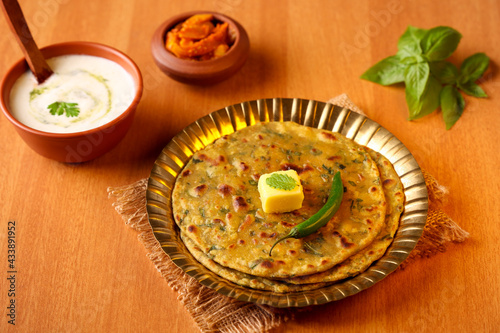 Palak paratha butter on spinach paratha , parantha ,chapati Indian flatbread roti made from spinach served in golden plate with yogurt mint dip, mango pickle, North Indian breakfast food Delhi India.