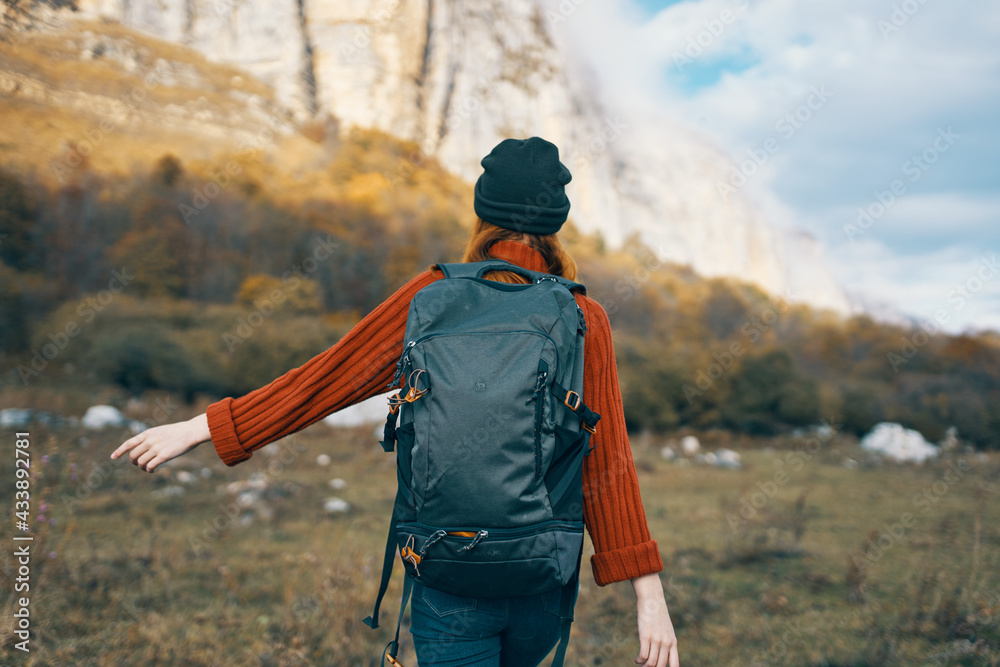 woman in a warm hat with a backpack on her back and in a sweater outdoors in the mountains gesticulate with her hands