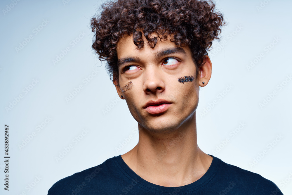Obraz premium guy with curly hair applies a black mask on his face cosmetology