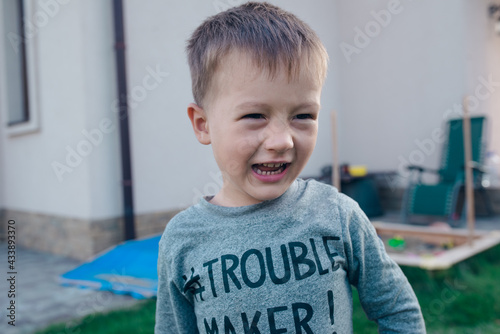 Bild auf Leinwand Mischievous boy in the yard is laughing leerily with Trouble Maker lettering on the T-shirt