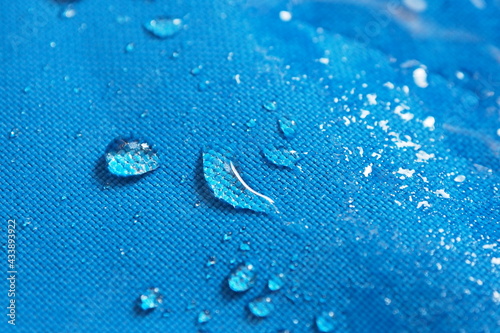 Closeup of water drops on bright blue fabric with waterproof design to protect fabric of the cloth from humidity and to offer easy cleaning to users Fabric texture with design and background concept