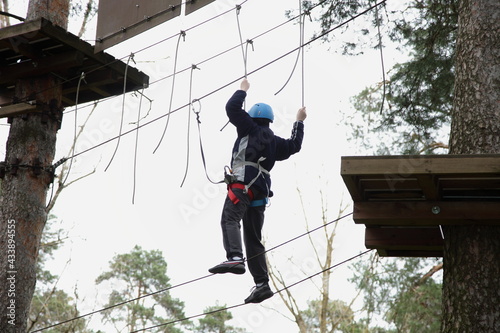 Tightrope walker boy in helmet and safety equipment on European outdoor forest rope park at spring summer day - climbing sports active recreation