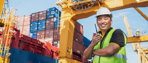 portrait photo of happy Asian logistics worker with radio transceiver working in port shipping containers. logistics, sea transportation,  commercial and logistics business concept