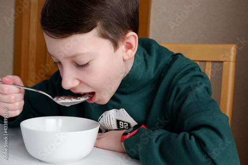 Boy in green sweatshirt having breakfast with chocolate balls with milk