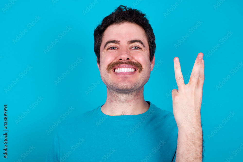 young handsome Caucasian man with moustache wearing blue t-shirt against blue background smiling and looking friendly, showing number three or third with hand forward, counting down young handsome Caucasian man with moustache wearing blue t-shirt against blue background smiling and looking friendly, showing number three or third with hand forward, counting down