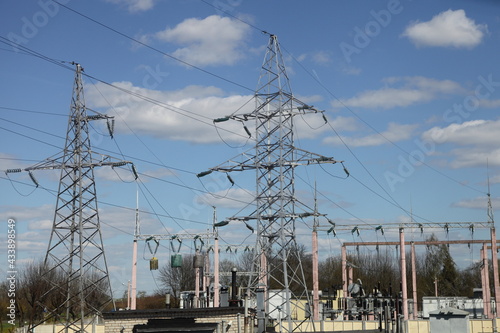 Two large high voltage electric power mast of an overhead air power line closeup, steel electricity pylons with wires and insulators on blue sky background at spring, traditional electrical energy net