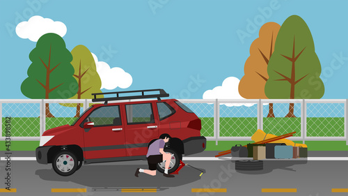 A man changes a spare tire on a motorway. Use a jack to pry the car up. Take all the luggage off the car on the side of the road. ฺBackground of steel wire wall separating the grassland and blue sky. 
